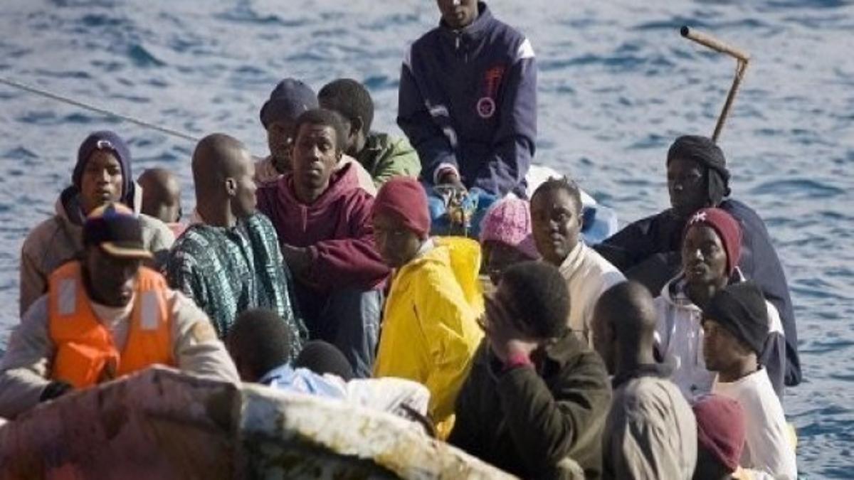 Groupe de personnes entassées sur une embarcation en mer, portant des vêtements de protection et gilets de sauvetage, illustrant une traversée migratoire dans des conditions précaires