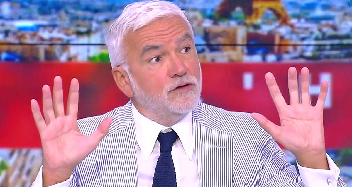 Animateur de télévision en plein débat sur un plateau d’information, levant les mains dans un geste d’explication face à des interlocuteurs, expression surprise et ambiance tendue en direct avec décor de studio en arrière-plan