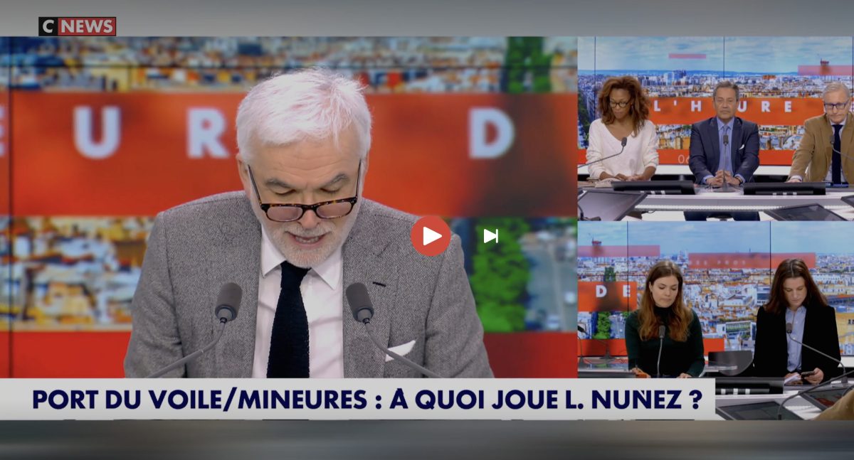 Plateau de télévision en direct avec un animateur lisant ses notes, entouré de chroniqueurs en duplex, ambiance tendue après une erreur évoquée à l’antenne sur un débat lié au port du voile chez les mineures