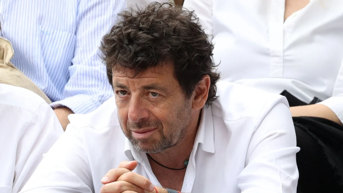 Homme assis au milieu d’un public, regard concentré et mains jointes, expression sérieuse, ambiance d’événement ou de débat public