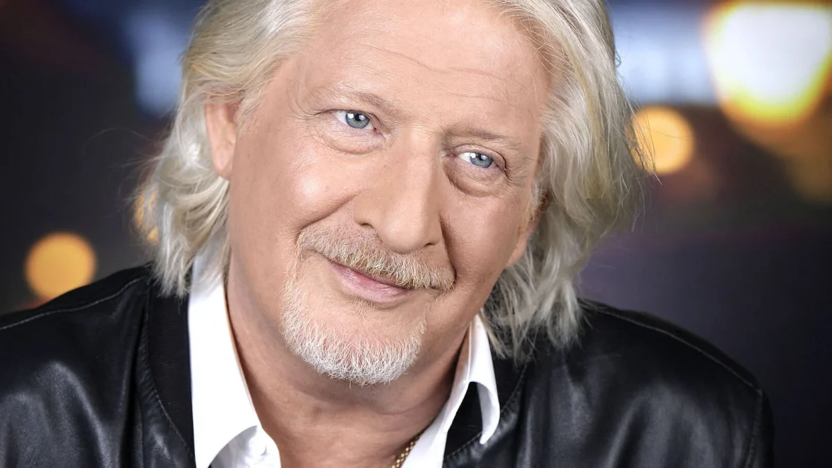 Homme aux cheveux gris et regard bleu, sourire léger et visage apaisé, portrait rapproché sur fond flou lumineux