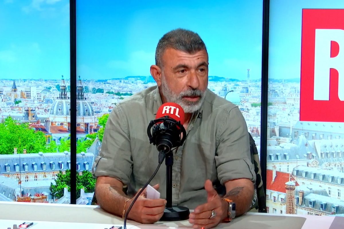Homme barbu d’âge mûr s’exprimant face à un micro dans un studio radio avec une vue urbaine en arrière-plan, illustrant un témoignage sur les dangers d’internet pour les enfants et la lutte contre les prédateurs en ligne
