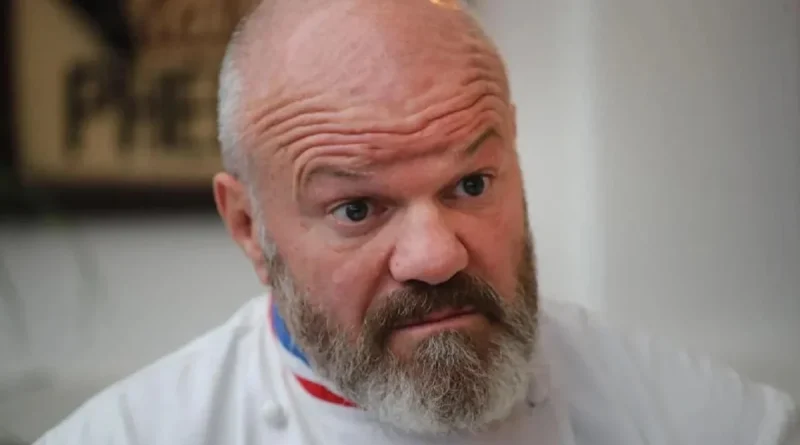 Chef cuisinier en tenue blanche avec col tricolore affichant une expression de surprise et d’incompréhension, regard intense face à une situation inattendue en cuisine