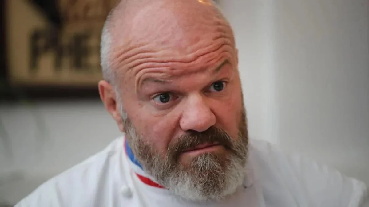 Chef cuisinier en tenue blanche avec col tricolore affichant une expression de surprise et d’incompréhension, regard intense face à une situation inattendue en cuisine