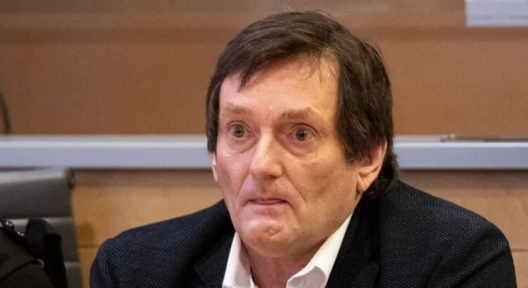 Homme assis dans une salle d’audience au visage marqué et au regard fixe, portant une veste sombre, illustrant une comparution judiciaire liée à une affaire médiatisée