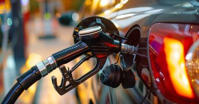 Pistolet de carburant inséré dans le réservoir d’une voiture lors d’un plein en station-service, éclairage urbain en arrière-plan illustrant la hausse du prix de l’essence