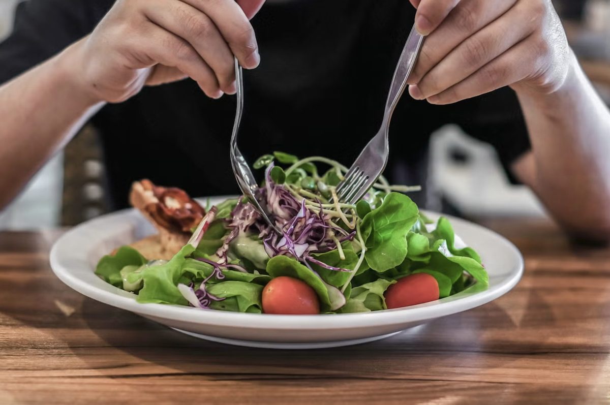 Personne en train de manger une salade composée au restaurant avec des crudités fraîches, des tomates cerises et du poulet, illustrant un plat simple souvent choisi par défaut mais parfois jugé décevant
