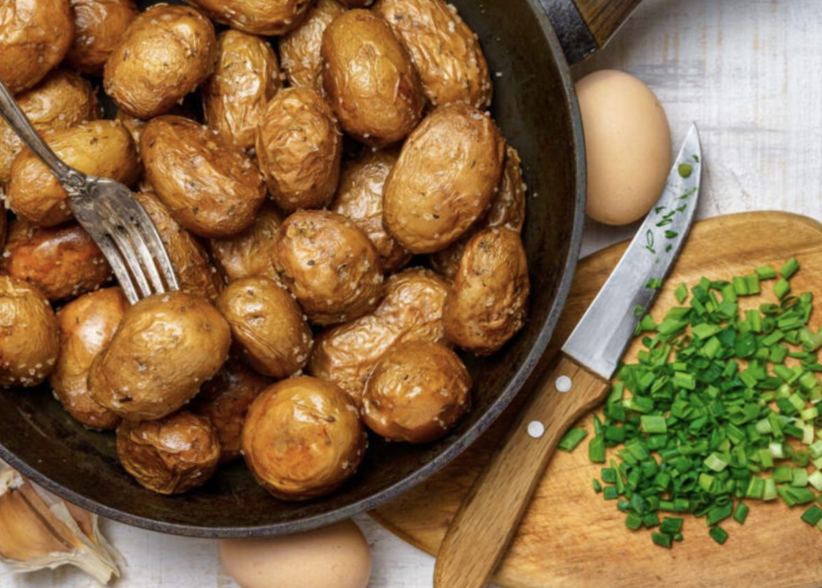 Pommes de terre grenaille dorées et croustillantes dans une poêle avec ail, sel et herbes fraîches, accompagnées d’ingrédients sur une planche en bois, texture fondante et aspect appétissant