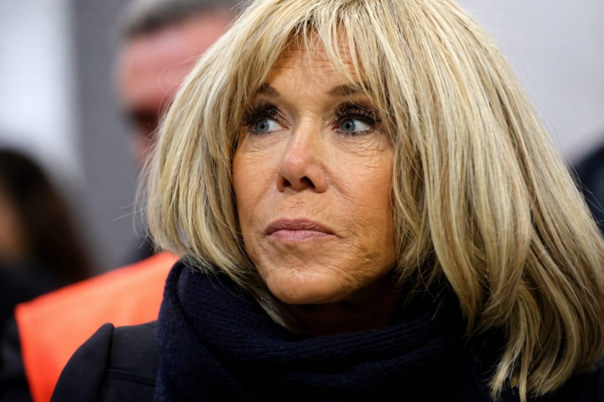 Portrait en gros plan d’une femme blonde au regard sérieux, portant une écharpe sombre, observant quelque chose hors champ dans un contexte public