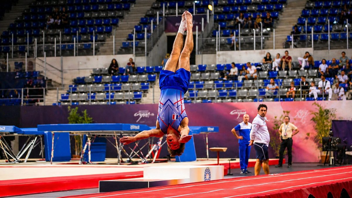 Gymnaste réalisant un saut acrobatique spectaculaire en tumbling sur une piste dynamique lors d’une compétition dans une salle sportive