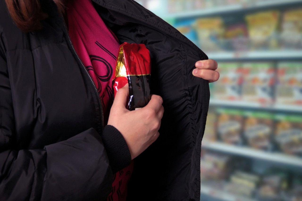 Personne dans un supermarché dissimulant discrètement un produit alimentaire sous sa veste, scène illustrant le vol à l’étalage lié à la précarité