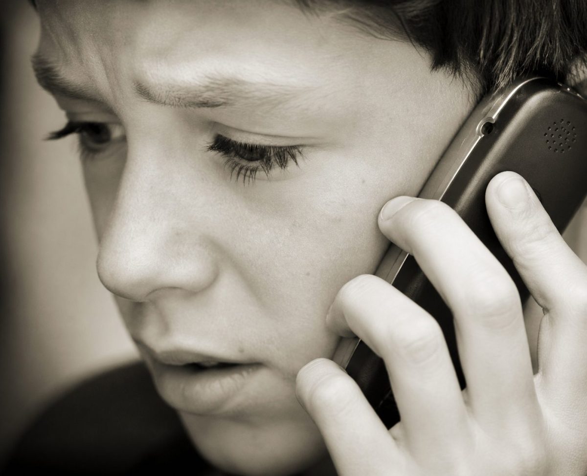 Adolescent inquiet au téléphone en gros plan en noir et blanc, appelant les forces de l’ordre pour signaler une situation dangereuse impliquant sa mère, illustration d’un fait divers en Moselle