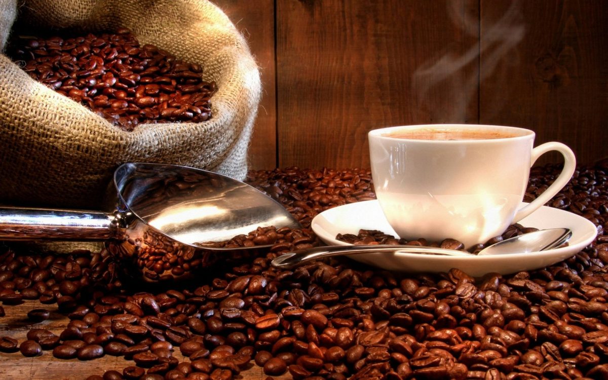 Tasse de café fumante posée sur une soucoupe blanche entourée de grains de café torréfiés et d’un sac en toile rempli de café, illustration des bienfaits et effets de la caféine sur la santé et le cerveau
