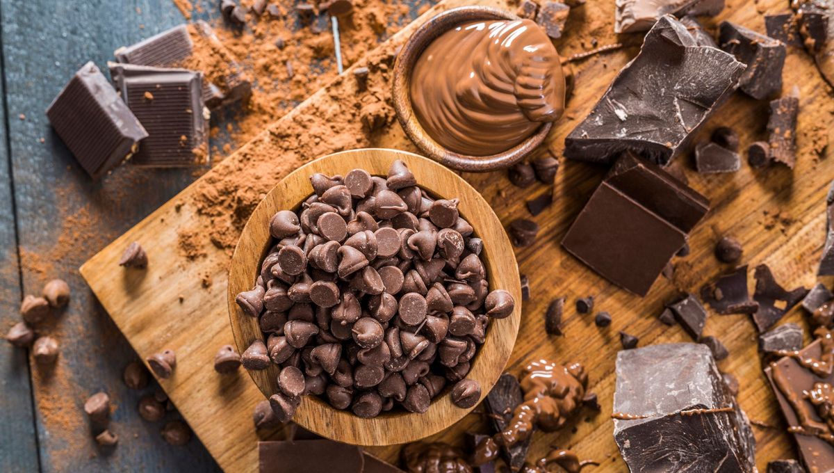Différents types de chocolat noir et cacao présentés sur une table en bois avec copeaux, poudre de cacao et pépites de chocolat, illustration des recherches scientifiques sur les bienfaits et les effets du chocolat sur la santé