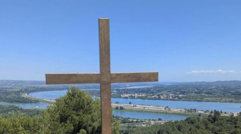 Grande croix métallique installée au sommet d’une colline dans le Gard avec vue panoramique sur une rivière et la campagne environnante, illustrant la polémique autour de la laïcité et des symboles religieux dans l’espace public en France.