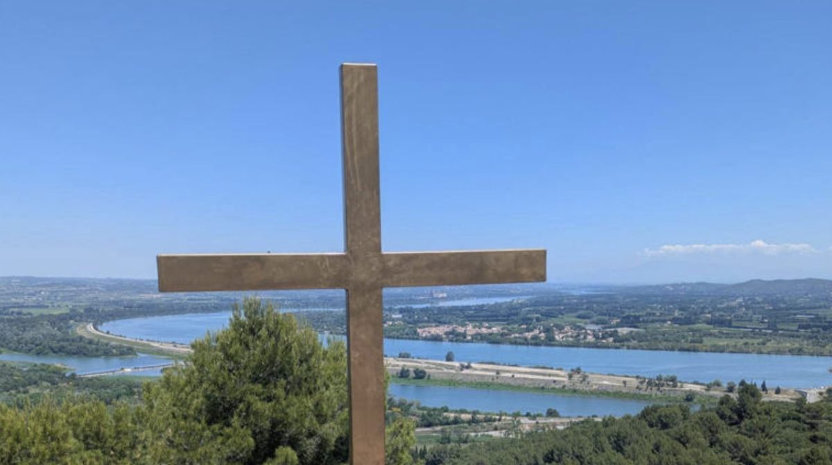 Grande croix métallique installée au sommet d’une colline dans le Gard avec vue panoramique sur une rivière et la campagne environnante, illustrant la polémique autour de la laïcité et des symboles religieux dans l’espace public en France.