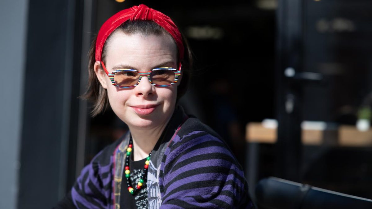 portrait d’Éléonore Laloux portant des lunettes colorées et un bandeau rouge, engagée dans la défense des droits des personnes porteuses de trisomie 21 et de l’inclusion des personnes handicapées en France