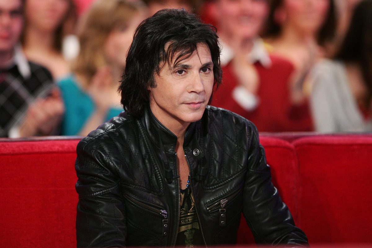 Jean-Luc Lahaye assis sur un canapé rouge lors d’une émission télévisée, portant une veste noire en cuir, dans un contexte de polémique autour de ses concerts programmés dans des mairies RN malgré les accusations de violences sexuelles visant le chanteur.