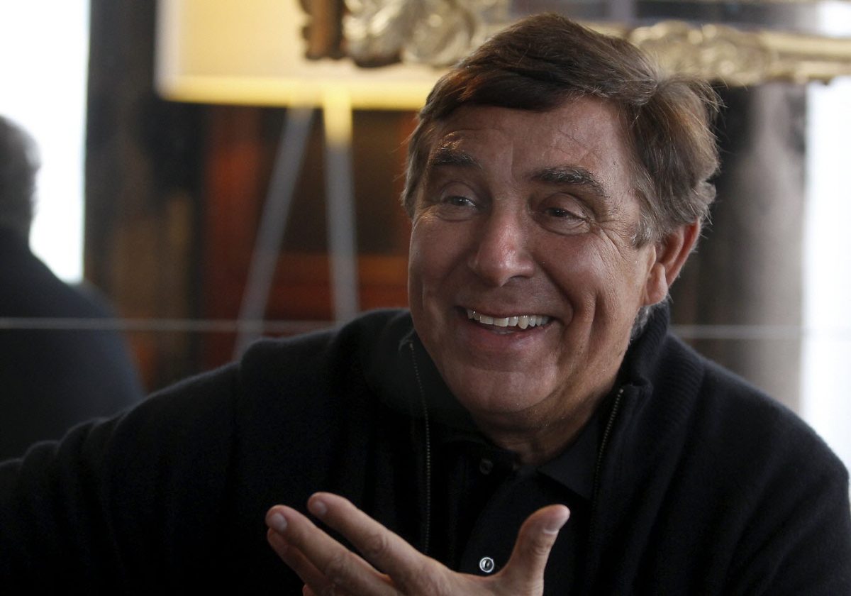 Animateur de télévision français souriant lors d’un entretien dans un intérieur élégant, illustration d’une carrière audiovisuelle exceptionnelle marquée par des émissions cultes et des décennies de succès à la télévision française.