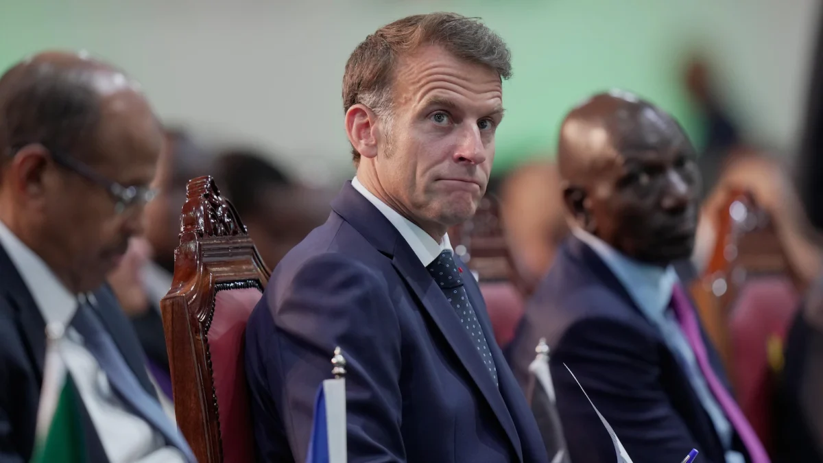 Président français assis lors d’un sommet international africain, entouré de responsables politiques et diplomatiques, avec une expression sérieuse dans un contexte de débat sur les investissements annoncés en Afrique.