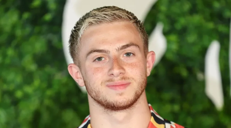 portrait du youtubeur Michou lors d’un événement public, avec un fond végétal vert et une expression neutre, illustration utilisée dans un article sur le scandale autour de son fast-food à Paris