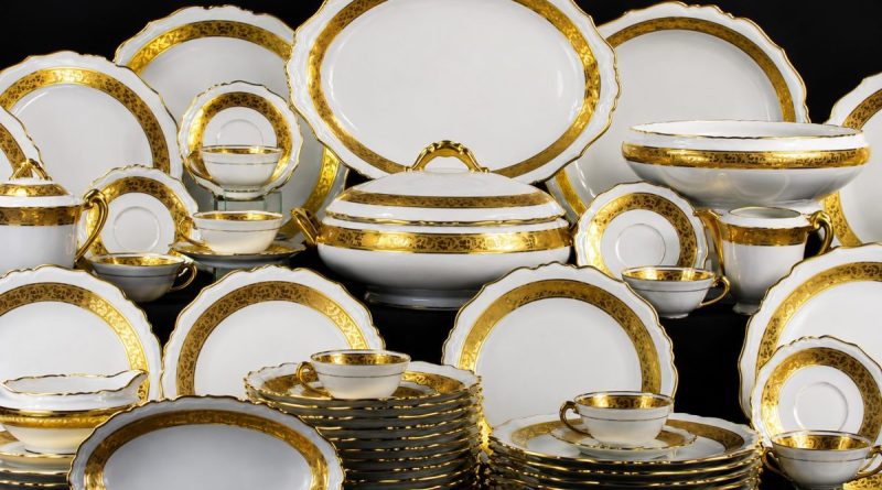 Service complet de Porcelaine de Limoges blanche et dorée présenté sur fond noir, composé d’assiettes, tasses, soupières et plats raffinés aux finitions élégantes inspirées du luxe français.