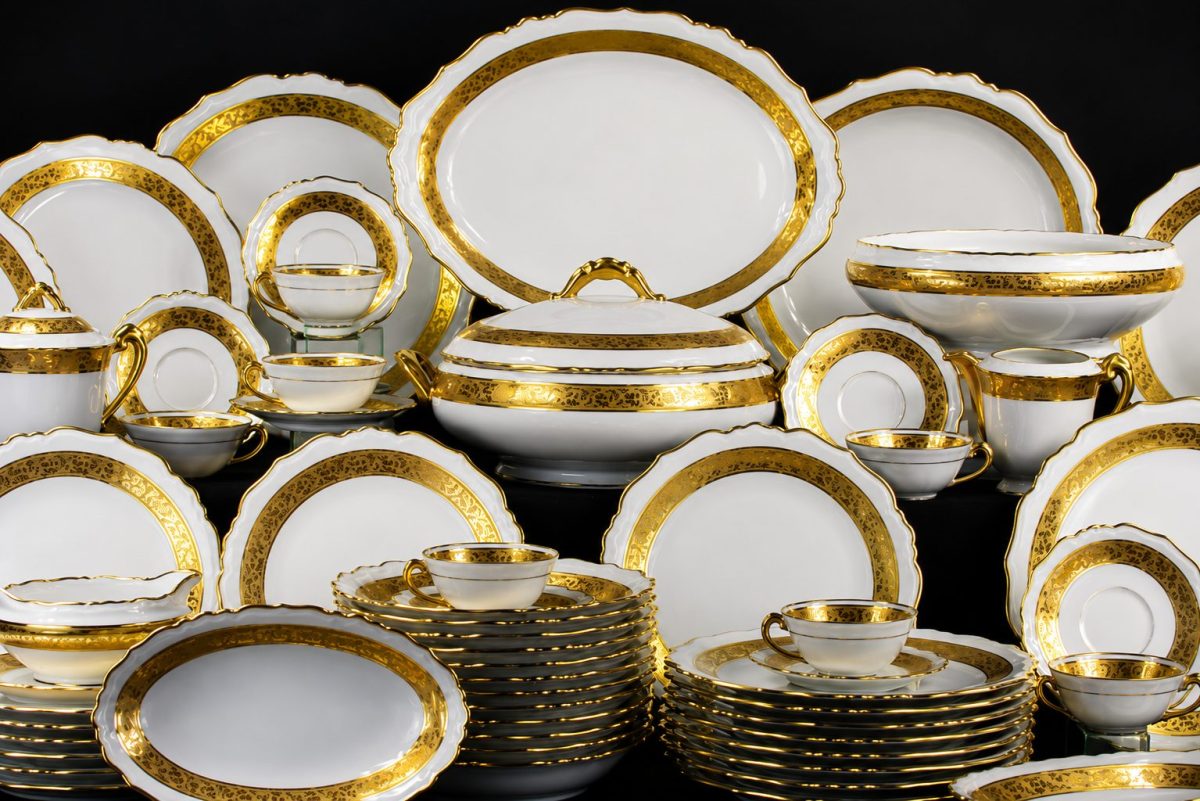 Service complet de Porcelaine de Limoges blanche et dorée présenté sur fond noir, composé d’assiettes, tasses, soupières et plats raffinés aux finitions élégantes inspirées du luxe français.
