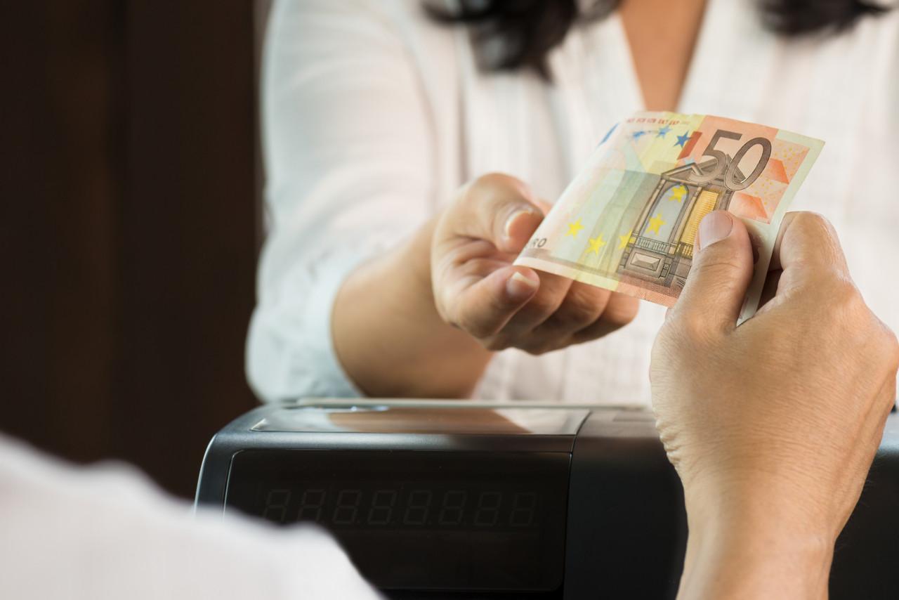 Client tendant un billet de 50 euros à un commerçant derrière une caisse de restaurant, scène illustrant un paiement en espèces et un possible refus de liquide, ambiance réaliste liée aux règles de paiement en France.