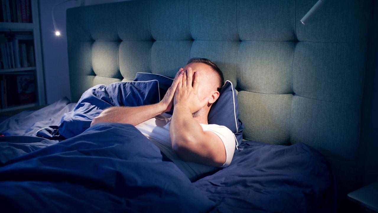 Homme allongé dans son lit en pleine nuit, les mains sur le visage après un réveil nocturne, illustration de l’insomnie et des réveils fréquents vers 4 heures du matin liés au stress et aux troubles du sommeil.