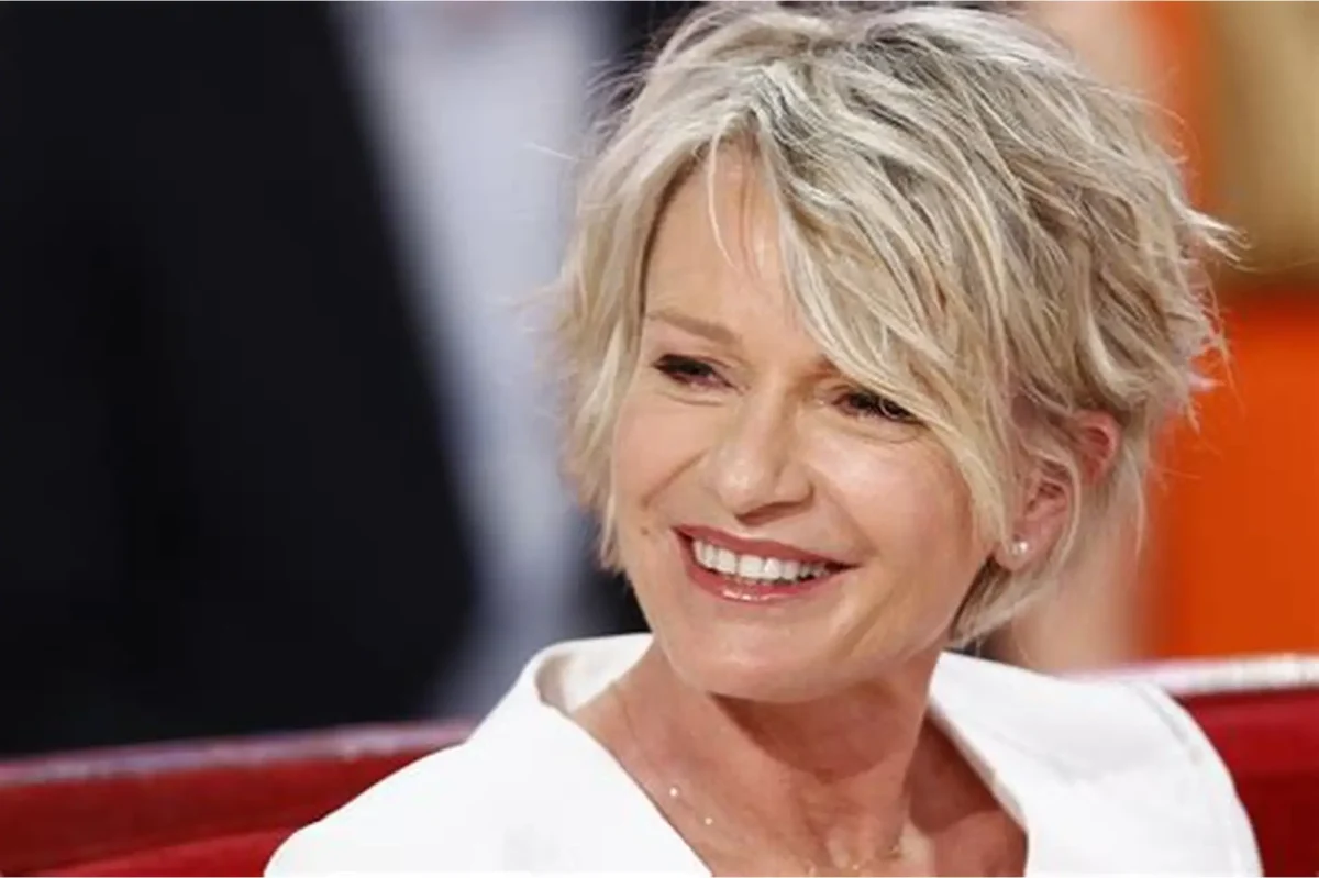 Portrait de Sophie Davant souriante sur un plateau de télévision, cheveux blonds courts et tenue claire élégante, illustration d’un article sur la médecine esthétique, les injections et le vieillissement des célébrités à la télévision.