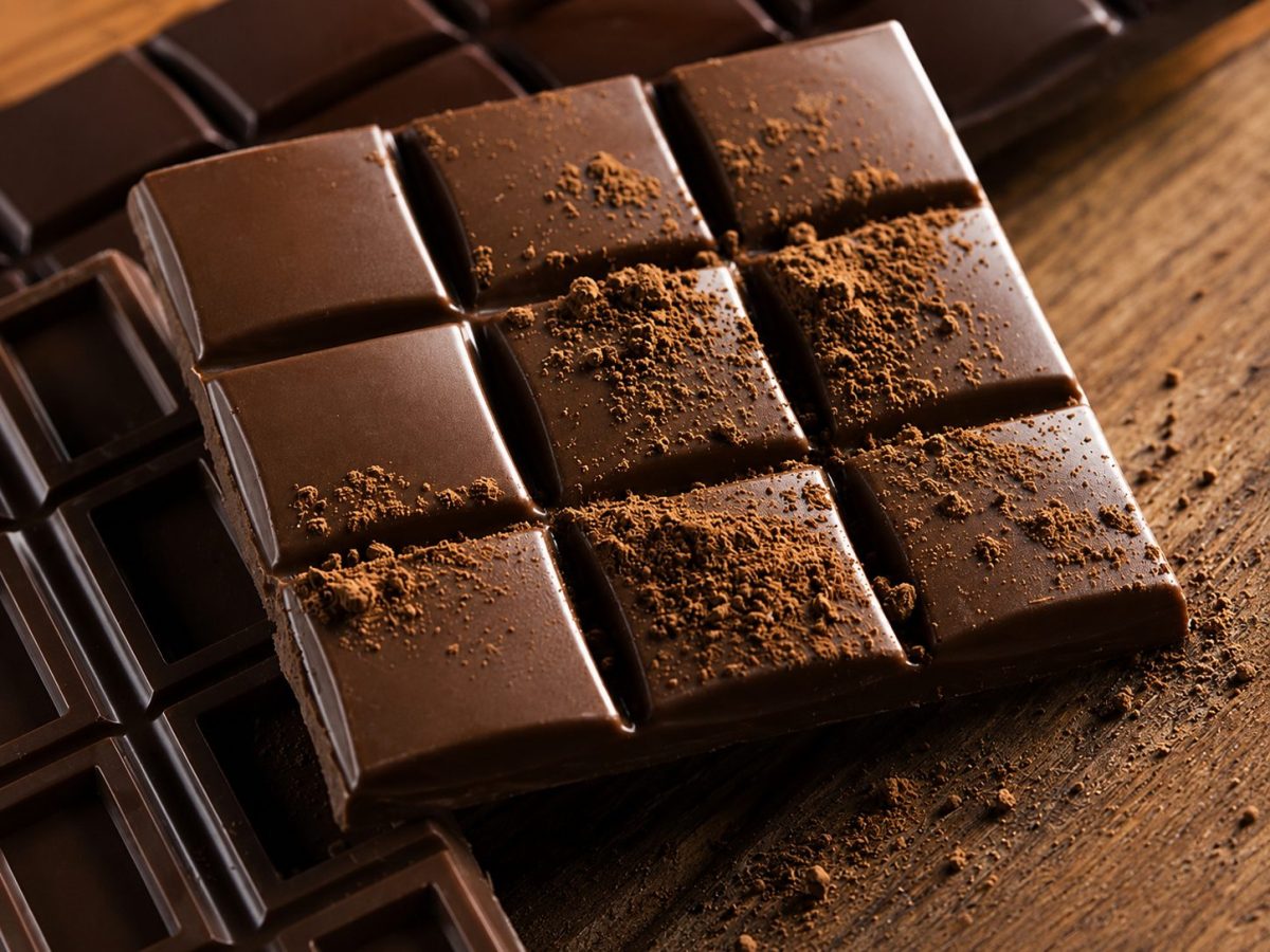 Tablette de chocolat noir recouverte de poudre de cacao sur une table en bois, illustration des antioxydants naturels du cacao et des bienfaits potentiels du chocolat noir pour la santé