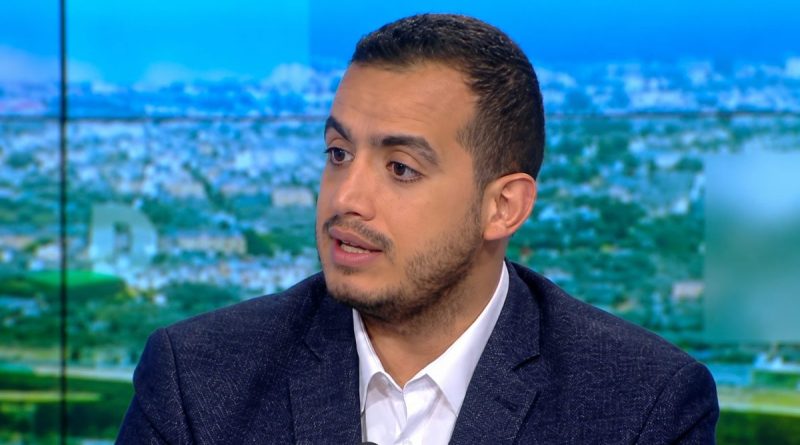 Portrait d’un intervenant médiatique en costume sombre lors d’une émission de télévision, filmé en gros plan sur un plateau d’actualité avec un décor urbain flou en arrière-plan. L’image illustre une prise de parole publique dans le cadre d’un débat sur les médias, le pluralisme et les questions de société.