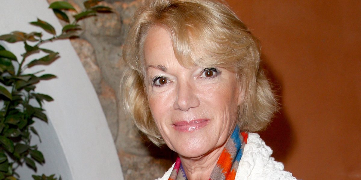 Portrait d’une femme blonde souriante lors d’un événement public en intérieur, regard dirigé vers l’objectif, dans une ambiance chaleureuse. Cette image illustre une actualité consacrée aux liens familiaux construits au fil du temps, à la transmission affective et à un projet d’adoption symbolique à l’âge adulte.