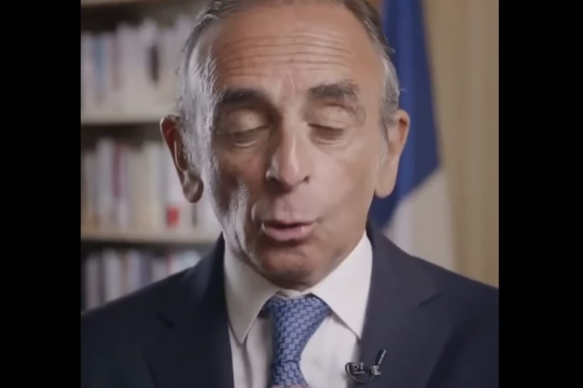 Portrait d’Éric Zemmour en costume et cravate lors d’une prise de parole filmée en intérieur, devant une bibliothèque et un drapeau français. Cette image illustre sa réaction aux violences et aux débordements survenus après la victoire du PSG en Ligue des champions, dans un contexte de débat sur l’insécurité et l’ordre public en France.