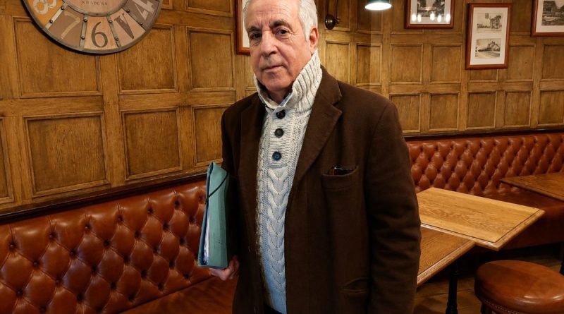 Homme retraité tenant une chemise de documents dans un café au décor en bois, illustrant les difficultés financières, le surendettement et les démarches judiciaires engagées contre une banque après l'accumulation de crédits à la consommation.