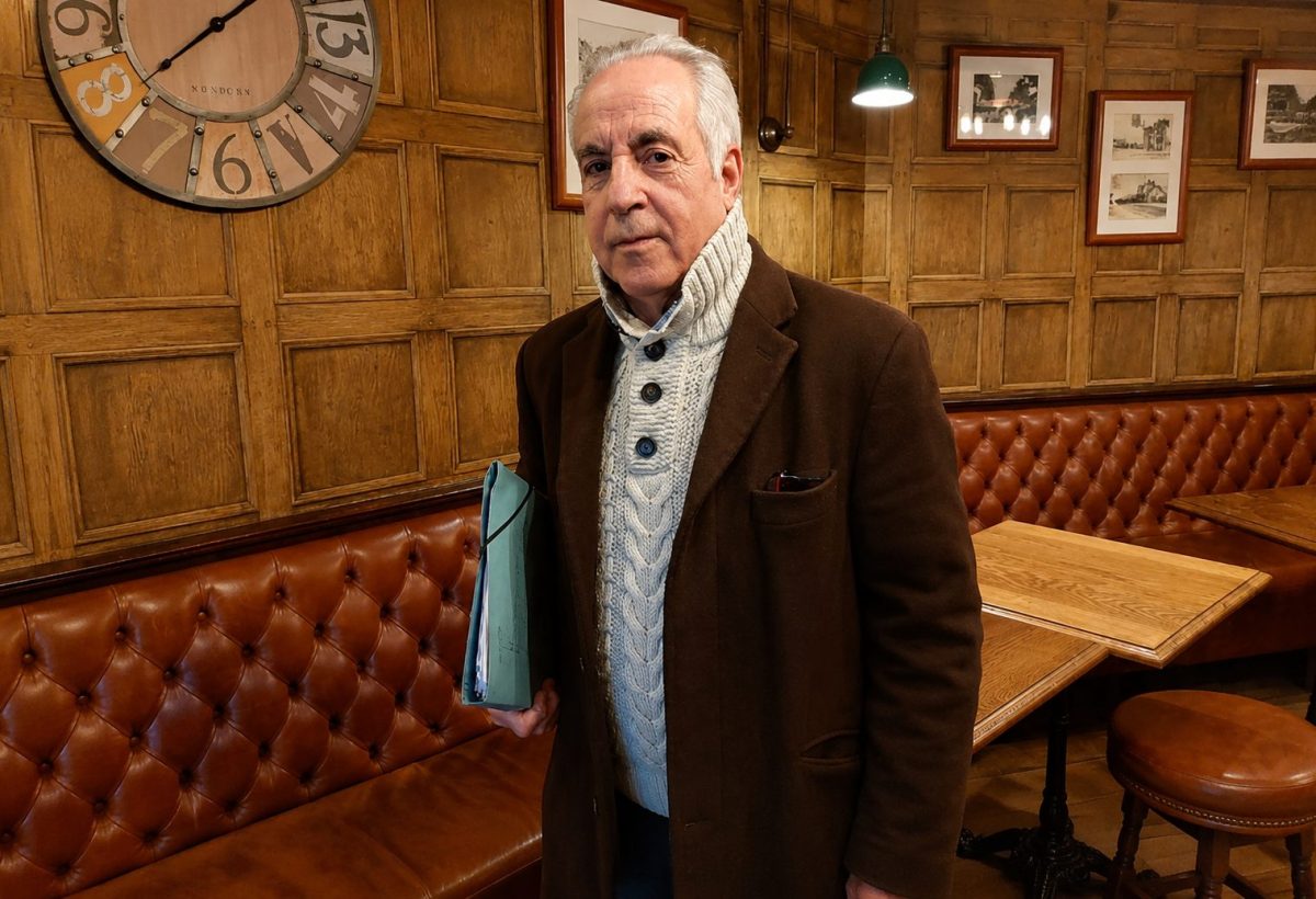 Homme retraité tenant une chemise de documents dans un café au décor en bois, illustrant les difficultés financières, le surendettement et les démarches judiciaires engagées contre une banque après l'accumulation de crédits à la consommation.
