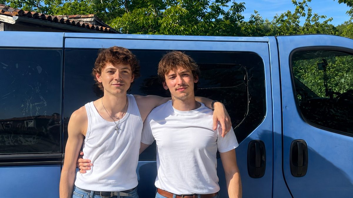 Deux jeunes hommes posent devant un van bleu lors de leur tournée à travers la France pour rencontrer des élus locaux. Cette image illustre la campagne itinérante menée dans le cadre de la recherche des 500 parrainages nécessaires à une candidature à l'élection présidentielle de 2027.