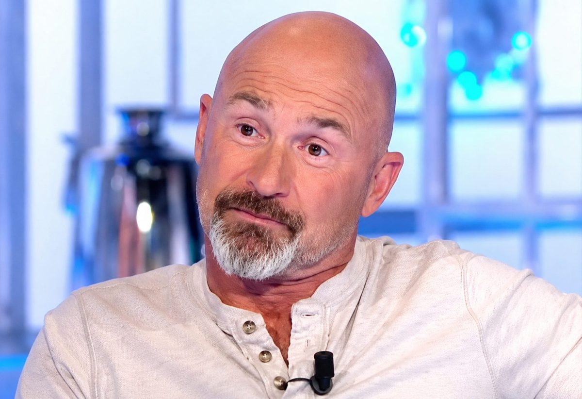 Homme chauve à la barbe grisonnante assis lors d'une interview télévisée, regard tourné vers son interlocuteur, dans un studio lumineux aux tons bleus. L'image illustre le parcours et la réussite d'une personnalité populaire du divertissement français devenue célèbre grâce à ses émissions de télévision et à un tube musical devenu culte.