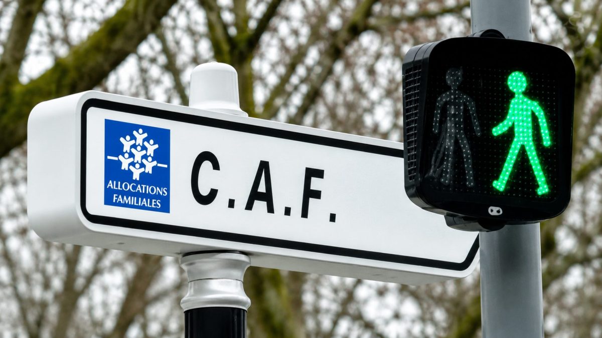 Panneau de la Caisse d'Allocations Familiales (CAF) à proximité d'un feu piéton vert, illustrant l'affaire d'un allocataire savoyard qui a reçu par erreur un courrier lui réclamant une dette de 1.062.026 euros à cause d'un dysfonctionnement informatique.