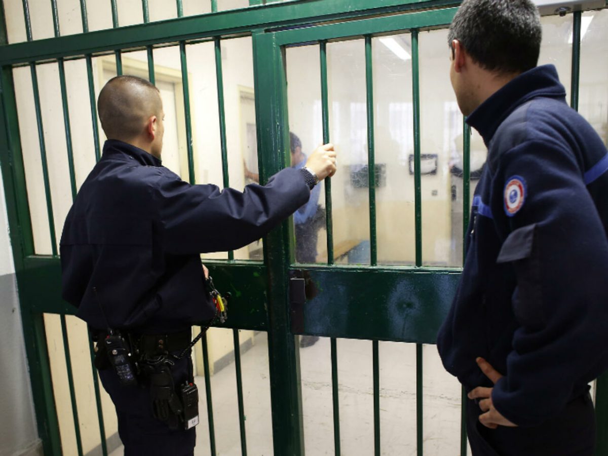 Deux surveillants pénitentiaires devant une porte sécurisée dans une prison française. Cette image illustre un article expliquant si les personnes détenues continuent de percevoir leur pension de retraite pendant leur incarcération conformément à la législation française.