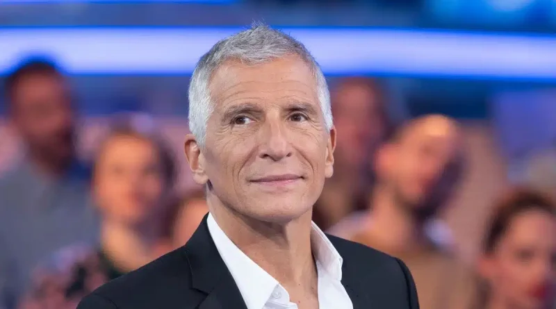 Portrait de l'animateur français Nagui sur un plateau de télévision. L'animateur est revenu sur un épisode de sa jeunesse au cours duquel il affirme avoir été refoulé de l'entrée d'un restaurant en raison de ses origines égyptiennes, un témoignage qui continue de susciter de nombreuses réactions.