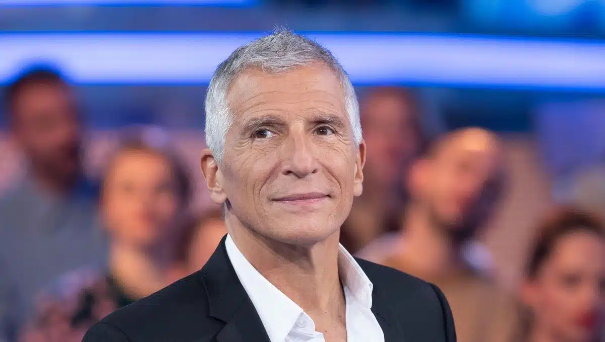 Portrait de l'animateur français Nagui sur un plateau de télévision. L'animateur est revenu sur un épisode de sa jeunesse au cours duquel il affirme avoir été refoulé de l'entrée d'un restaurant en raison de ses origines égyptiennes, un témoignage qui continue de susciter de nombreuses réactions.