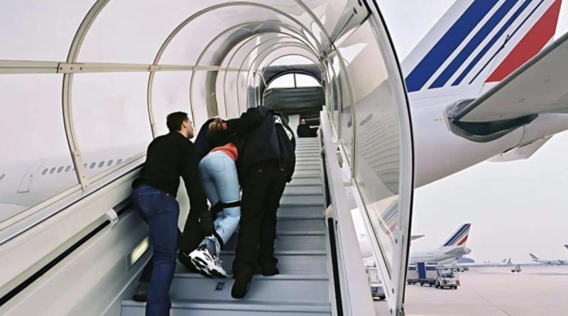 Un ressortissant algérien escorté par des agents des forces de l'ordre monte de force dans un avion dans le cadre d'une procédure d'expulsion liée à une OQTF après plusieurs refus d'embarquer vers l'Algérie.
