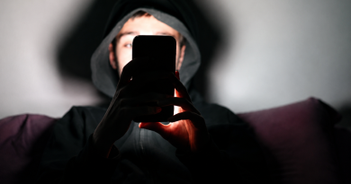 Jeune homme portant une capuche noire, plongé dans l’obscurité et regardant un smartphone dont la lumière éclaire son visage et ses mains, illustration évoquant l’isolement, la détresse psychologique et les échanges avec une intelligence artificielle comme ChatGPT.