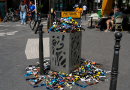 « Une poubelle publique déborde de lunettes de protection utilisées pour observer l’éclipse solaire, tandis que de nombreuses autres lunettes sont abandonnées sur le trottoir, illustrant la question des déchets, du gaspillage et de l’impact environnemental des objets utilisés pendant une très courte durée. »
