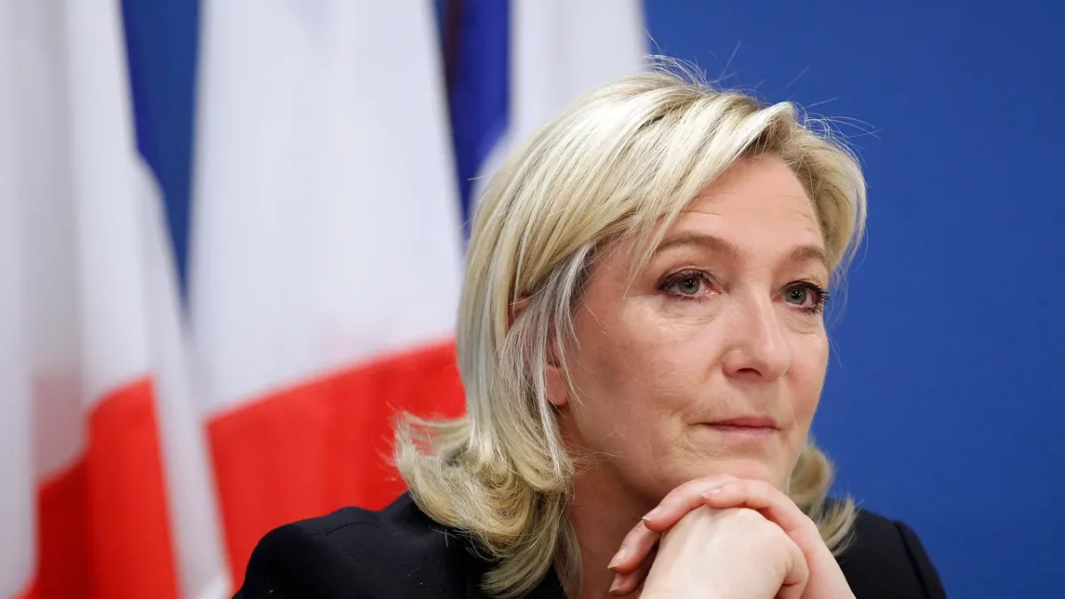 Portrait d’une femme politique française devant un drapeau tricolore, illustration du projet du RN visant à interdire le voile dans l’espace public et à sanctionner son port par une amende en cas de victoire à la présidentielle de 2027.