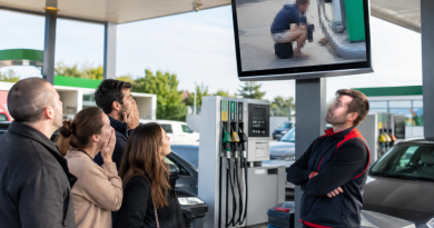 Illustration photoréaliste d'une station-service moderne avec plusieurs pompes à carburant. Des clients, visiblement choqués, regardent un écran diffusant une image volontairement floutée d'une scène d'incivilité, tandis qu'un employé observe la situation les bras croisés. Cette illustration accompagne un article consacré à la décision d'un Super U d'afficher une capture de vidéosurveillance pour dénoncer le comportement inapproprié d'un client.