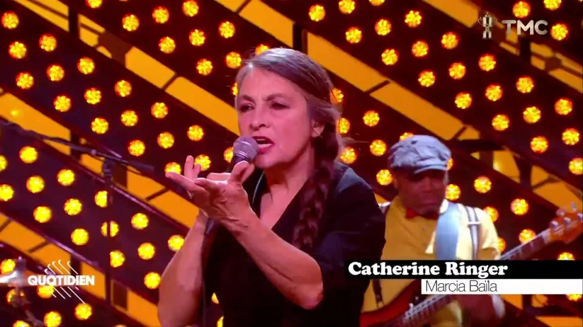 Catherine Ringer interprétant Marcia Baïla sur le plateau de Quotidien sur TMC, micro à la main devant ses musiciens.