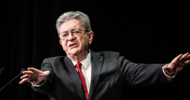 Responsable politique français en costume sombre et cravate rouge prenant la parole sur scène, illustration de la plainte visant Jean-Luc Mélenchon pour ses propos « tout blancs, tout moches »