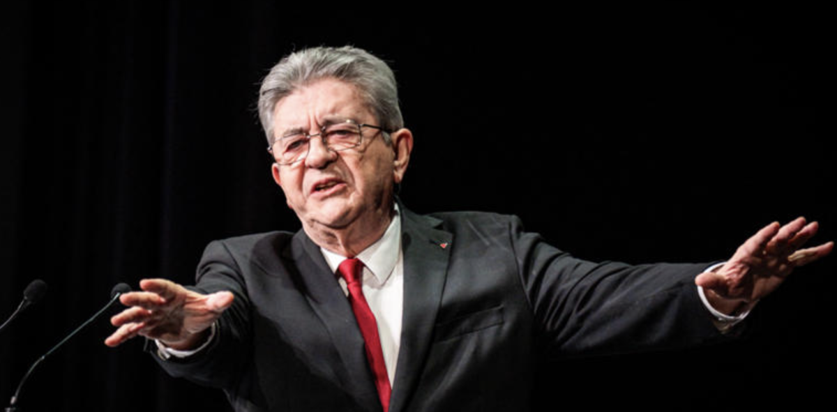 Responsable politique français en costume sombre et cravate rouge prenant la parole sur scène, illustration de la plainte visant Jean-Luc Mélenchon pour ses propos « tout blancs, tout moches »